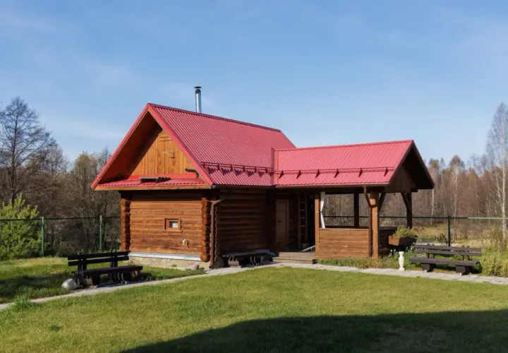 Drewniany domek letniskowy z czerwoną dachem, idealny na wypoczynek. Marzysz o takim miejscu? Sprawdź możliwości dofinansowanie na domek letniskowy!