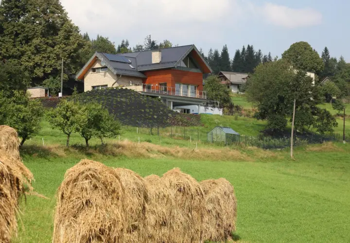 Nowoczesna zabudowa zagrodowa, kto może budować? Dom z panelami słonecznymi i drewnianą elewacją na wzgórzu, obok stogi siana.