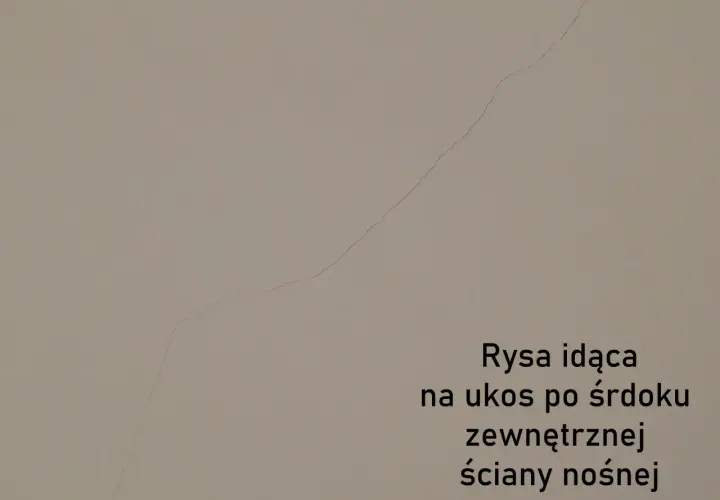 Pionowe pęknięcia ścian nośnych widoczne na jasnej powierzchni. Rysa biegnie ukośnie przez środek zewnętrznej ściany nośnej.