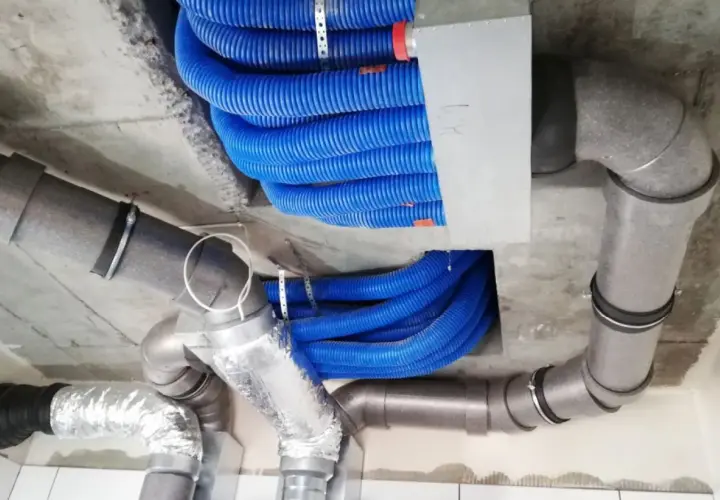 Instalacja rekuperacji w starym domu. Niebieskie przewody wentylacyjne i szare rury tworzą skomplikowany system pod sufitem.