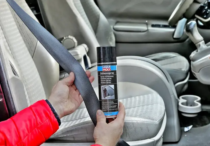 Ręce trzymające pas bezpieczeństwa i puszkę z napisem "Silikonspray". Preparat ten to olej silikonowy do paneli, który ułatwia konserwację wnętrza samochodu.