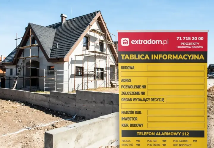 Tablica informacyjna budowy domu w trakcie prac, z widocznymi rusztowaniami. Na tablicy dane dotyczące budowy, adresu i kontaktów.