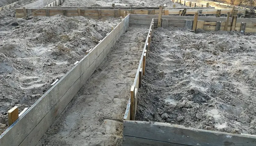 Wykonano wykopy pod fundamenty. Drewniane szalunki wyznaczają kształt przyszłego budynku na piaszczystym terenie budowy.