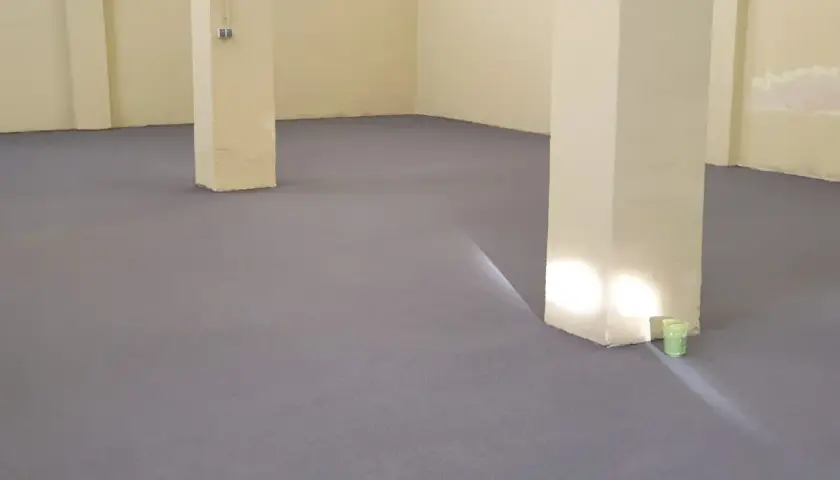 Nowa, szara posadzka betonowa w domu, z jasnymi filarami i żółtymi ścianami.