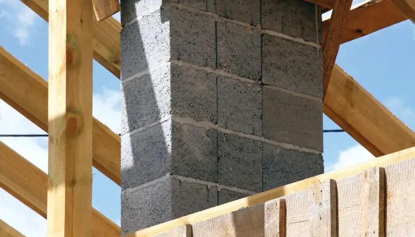 Solidny fundament pod komin systemowy, wznoszony z bloczków betonowych, otoczony drewnianą konstrukcją dachu.
