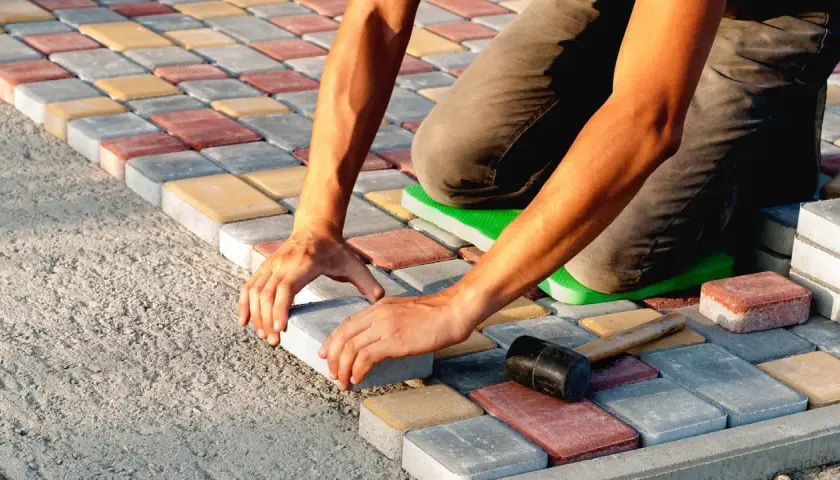 Ręce układają kolorową kostkę brukową, tworząc wzór. Praca wymaga precyzji i cierpliwości.