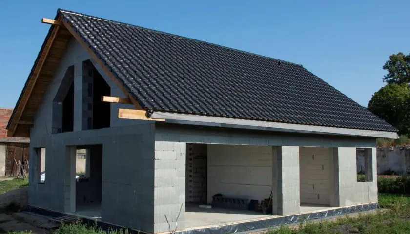 Dom w stanie surowym otwartym, z dachem pokrytym czarną dachówką, gotowy na dalsze prace budowlane.