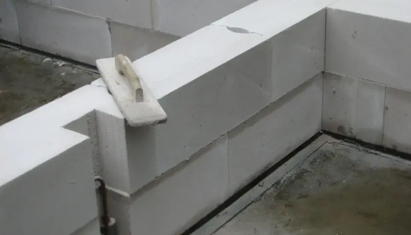Ściana z bloczków z betonu komórkowego w trakcie budowy. Na jednym z bloczków leży kielnia.