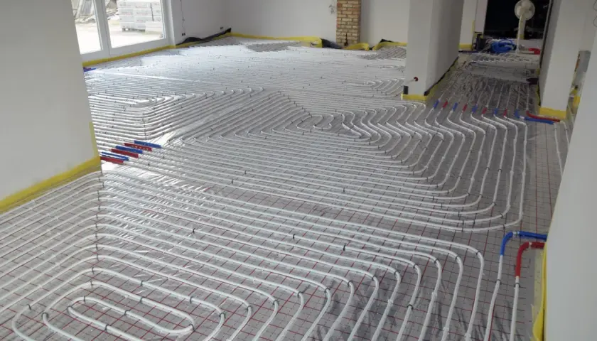 Instalacja ogrzewania podłogowego zasilanie podłogówki 40 stopni. Białe rurki ułożone w skomplikowany wzór na folii izolacyjnej.