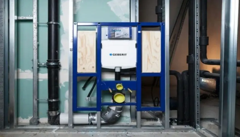 Montaż stelaża Geberit, widoczny podłączenie do odpływu. Instalacja hydrauliczna w trakcie budowy.