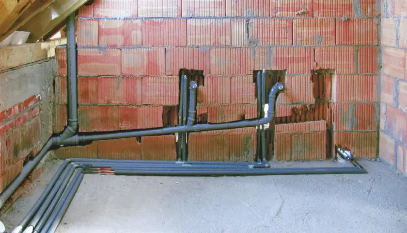 Instalacja hydrauliczna z rurami, zapewniająca minimalny spadek dla rury 160. Ściana z pustaków ceramicznych, podłoga betonowa, widoczne drewniane elementy konstrukcji dachu.