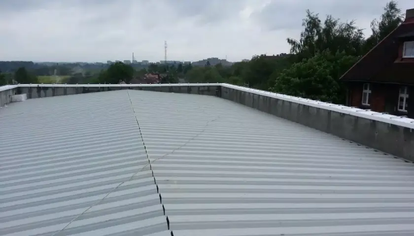 Szary, lekki dach płaski z blachy falistej, z widokiem na miasto w tle.