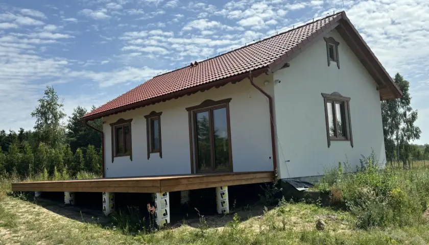 Nowy projekt domu drewnianego z tarasem, w otoczeniu zieleni.