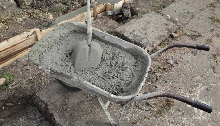 Taczka z betonem i łopatą czeka na wykonanie zbrojenia ławy fundamentowej.