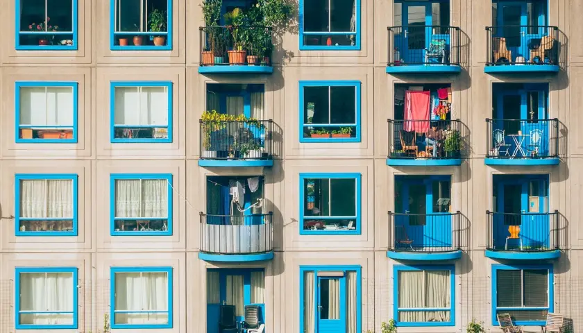 Elegancka loggia i balkon z niebieskimi ramami okiennymi, pełne zieleni i suszącego się prania, tworzą barwny obraz miejskiego życia.
