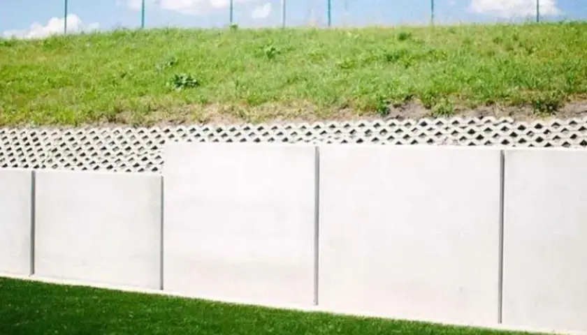 Solidny mur oporowy z betonowych płyt, nad nim ażurowa warstwa i zielone zbocze. Kara za mur oporowy? Raczej solidna konstrukcja.