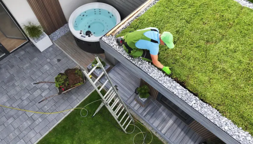 Pracownik pielęgnuje zielony dach, który jest przykładem powierzchni biologicznie czynnej. Obok jacuzzi i tarasu.