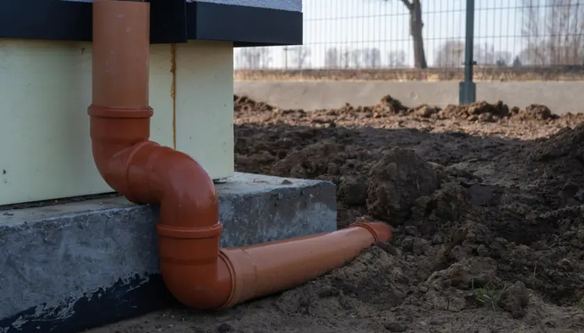 Pomarańczowe rury do odprowadzenia wody z rynien, połączone kolankami, biegną wzdłuż fundamentu domu i wkopane są w ziemię.