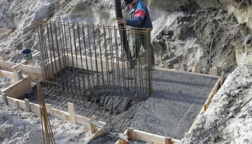 Betonowanie fundamentów. Pracownik wylewa beton do szalunku zbrojonego. Beton można lać do ok. +5°C.