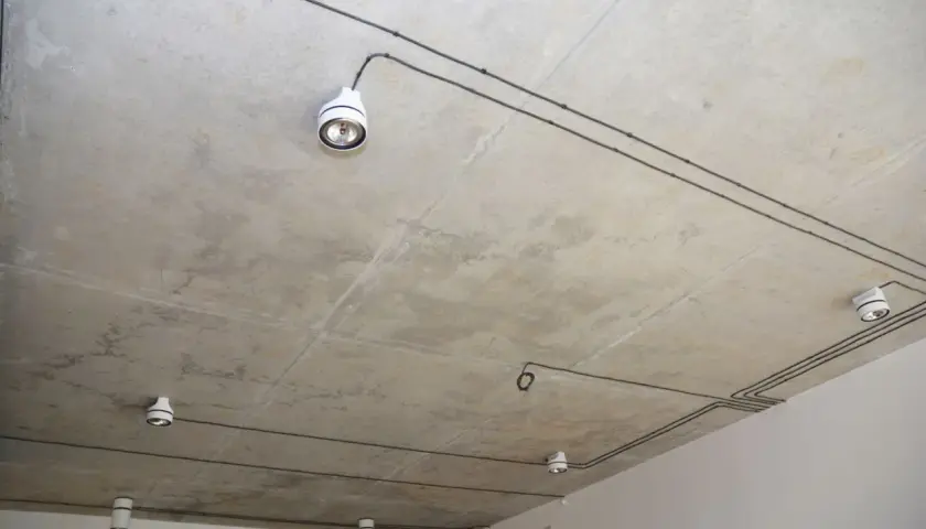 Nowoczesna instalacja elektryczna natynkowa na betonowym suficie z kilkoma białymi oprawami oświetleniowymi.