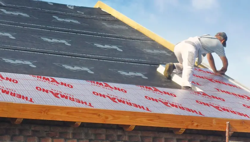 Pracownik montuje materiał izolacyjny na dachu, zapewniając ocieplenie dachu od zewnątrz.