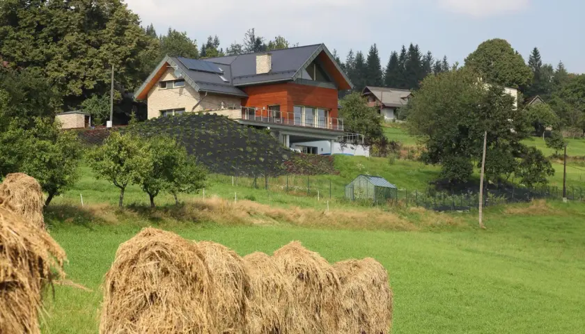 Nowoczesna zabudowa zagrodowa, kto może budować? Dom z panelami słonecznymi i drewnianą elewacją na wzgórzu, obok stogi siana.