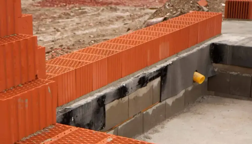 Budowa domu, widoczne pomarańczowe pustaki ceramiczne. Trwa układanie ścian fundamentowych, zastanawiasz się, ile suporexu na m2 będzie potrzebne?
