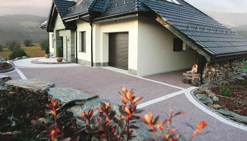 Piękny podjazd do domu z kostki brukowej, otoczony kamieniami i zielenią.