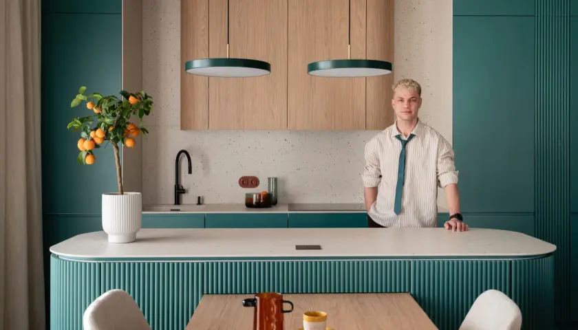 Nowoczesna kuchnia z turkusowymi frontami i drewnianymi panelami. Na blacie stoi drzewko pomarańczowe. W tle mężczyzna w koszuli.