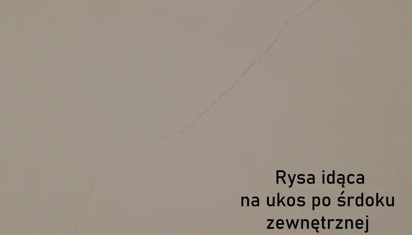 Pionowe pęknięcia ścian nośnych widoczne na jasnej powierzchni. Rysa biegnie ukośnie przez środek zewnętrznej ściany nośnej.