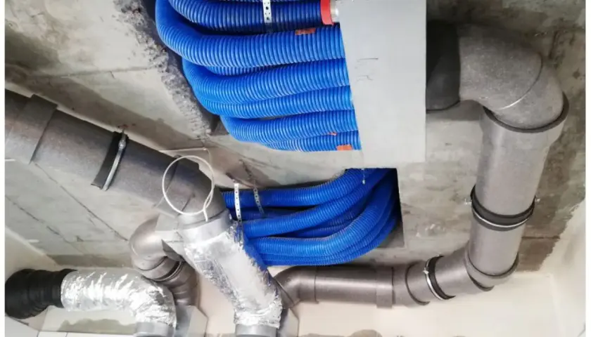 Instalacja rekuperacji w starym domu. Niebieskie przewody wentylacyjne i szare rury tworzą skomplikowany system pod sufitem.