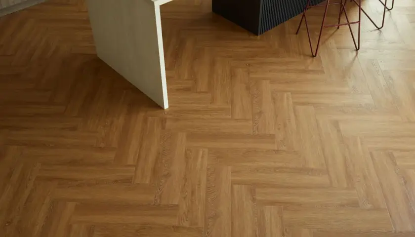 Drewnopodobne panele winylowe ułożone we wzór jodełki. Pokazują, jak układać panele winylowe, tworząc elegancką podłogę w kuchni.