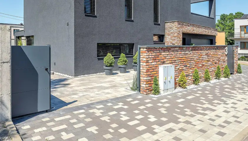 Nowoczesny dom z ceglanym murem i bramą. Podjazd i chodnik wykonane z kostki brukowej rodzaje w geometryczny wzór.