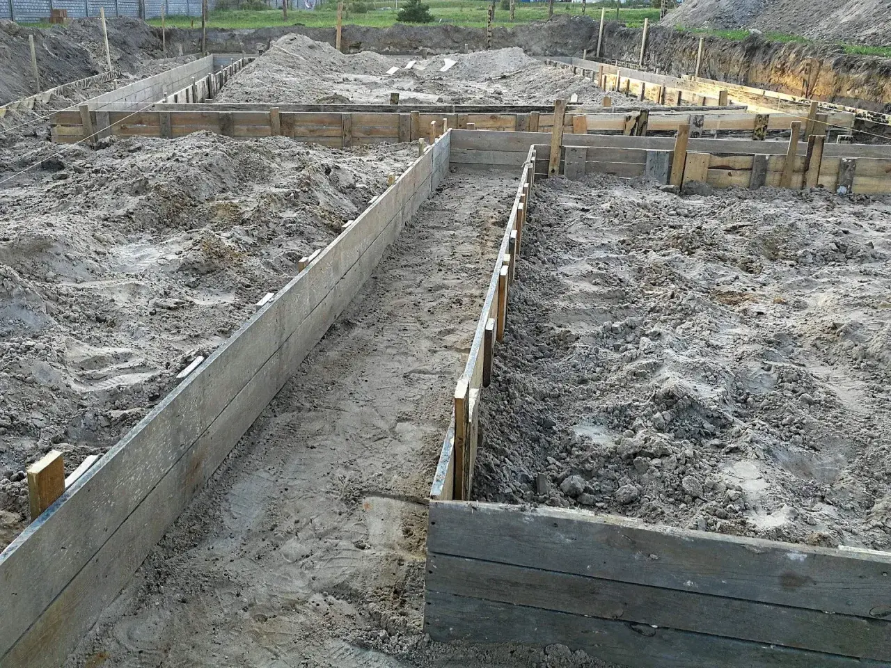 Wykonano wykopy pod fundamenty. Drewniane szalunki wyznaczają kształt przyszłego budynku na piaszczystym terenie budowy.