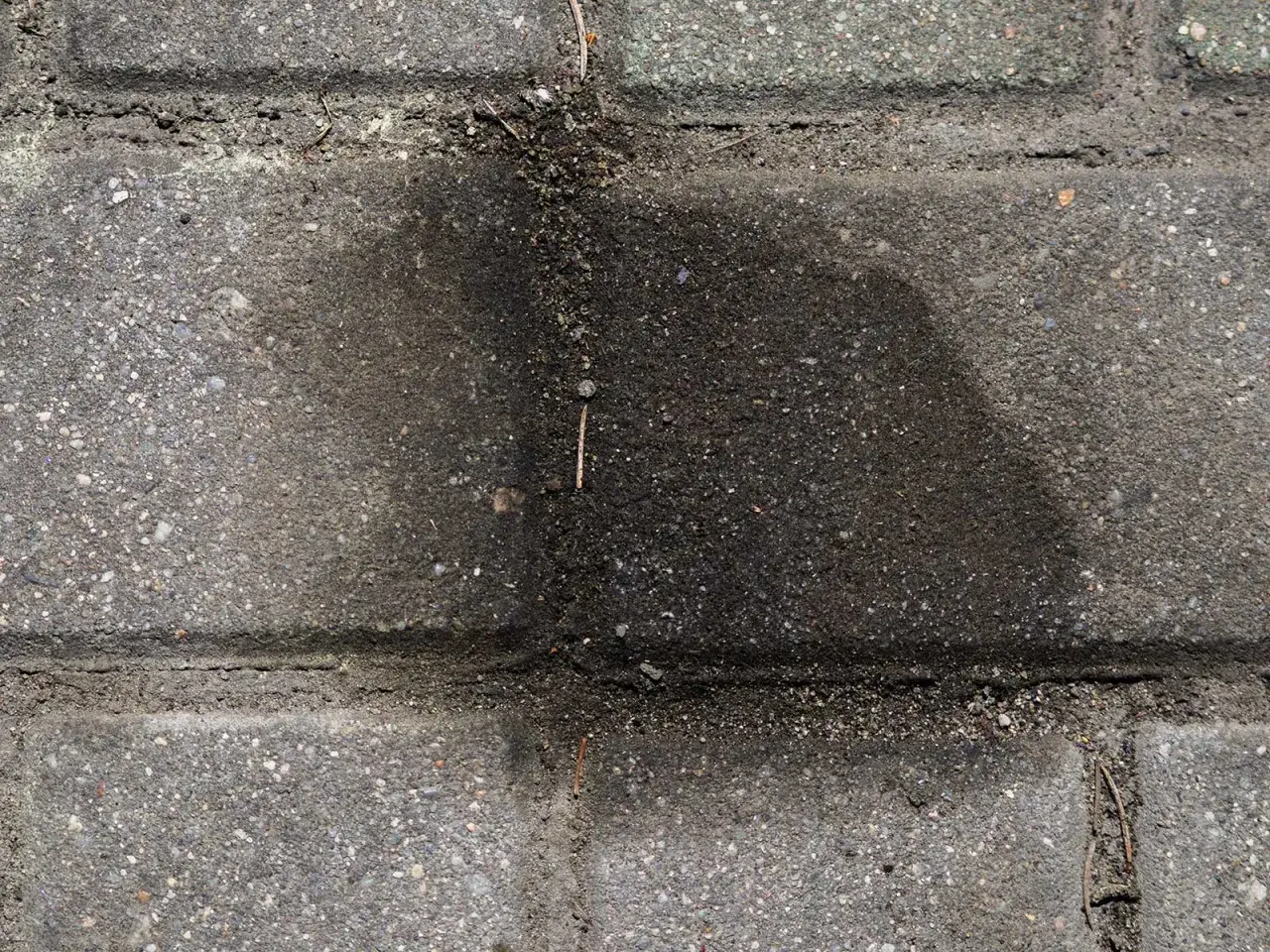 Stare plamy z oleju na kostce brukowej tworzą ciemny, rozlany kształt, świadcząc o dawnych wyciekach.