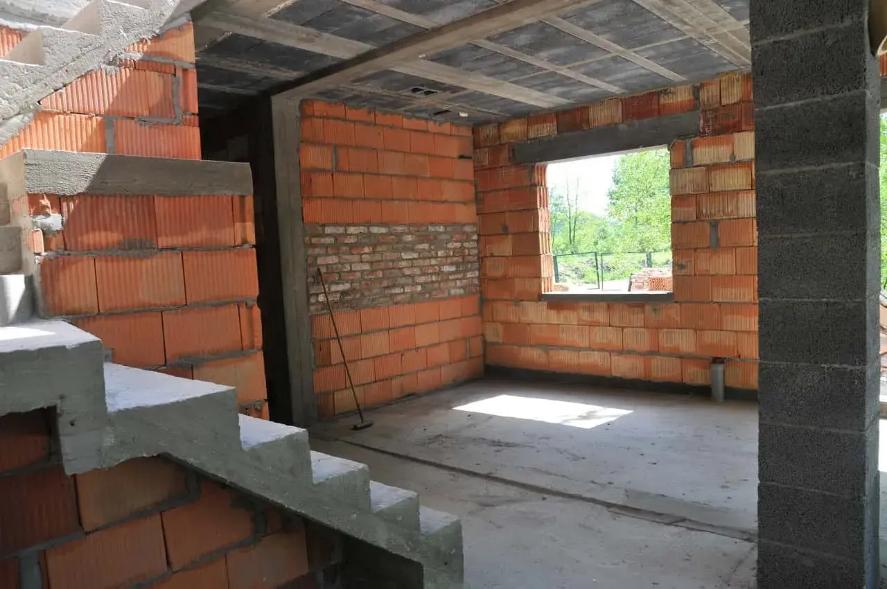 Trwa przekształcenie budynku gospodarczego na mieszkalny. Widoczne schody, ściany z pustaków ceramicznych i betonowy słup.