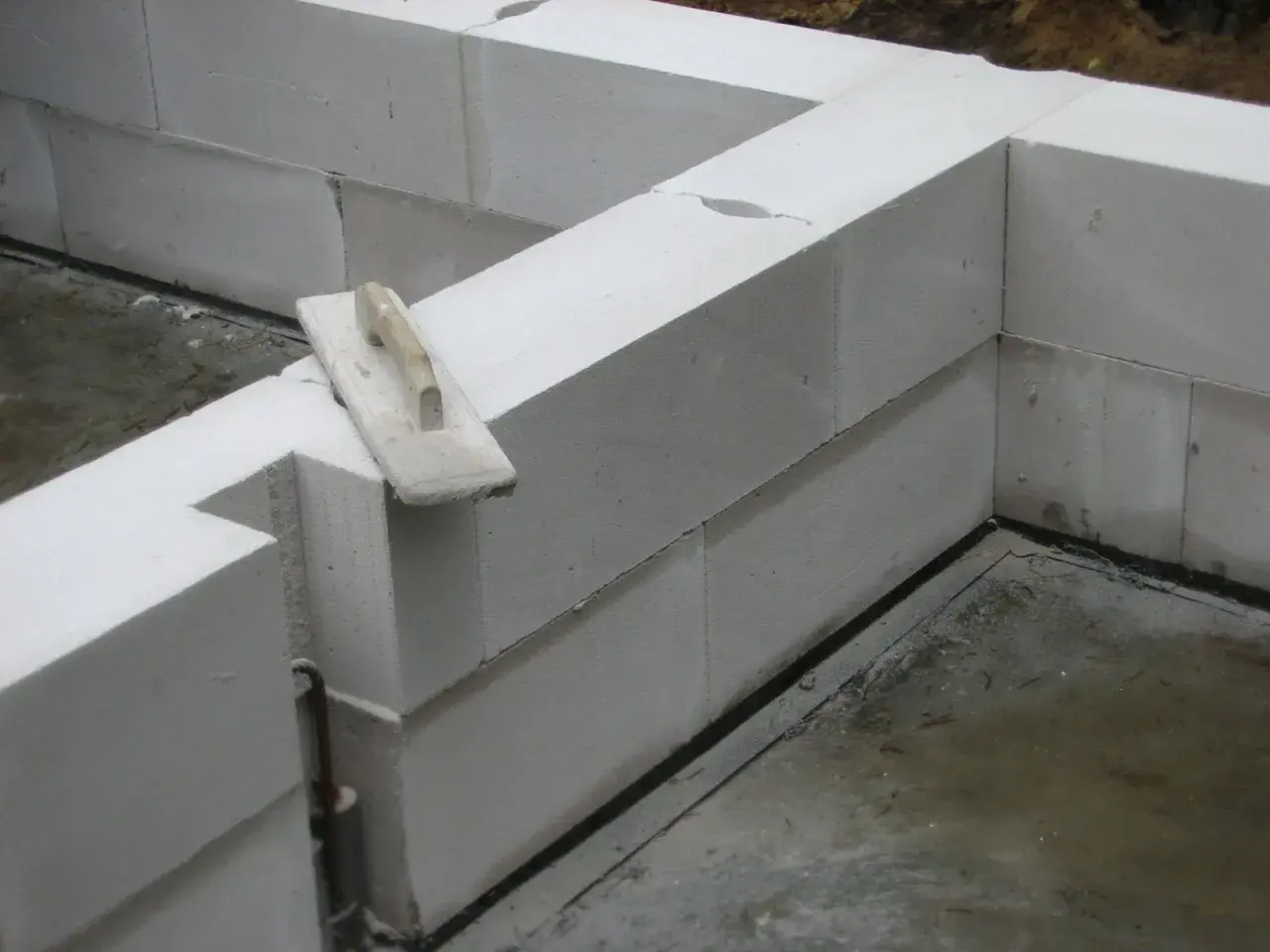 Ściana z bloczków z betonu komórkowego w trakcie budowy. Na jednym z bloczków leży kielnia.