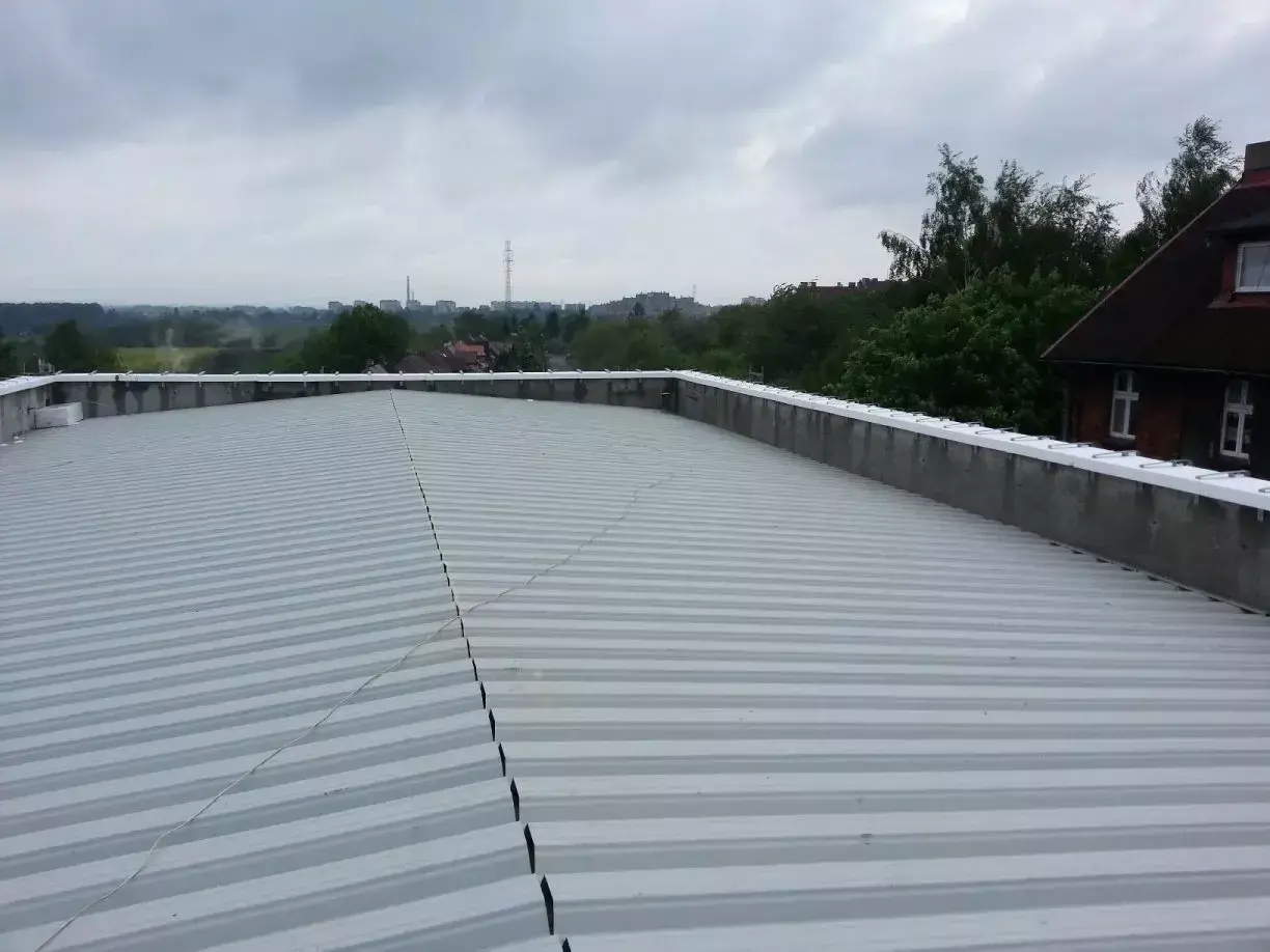 Szary, lekki dach płaski z blachy falistej, z widokiem na miasto w tle.