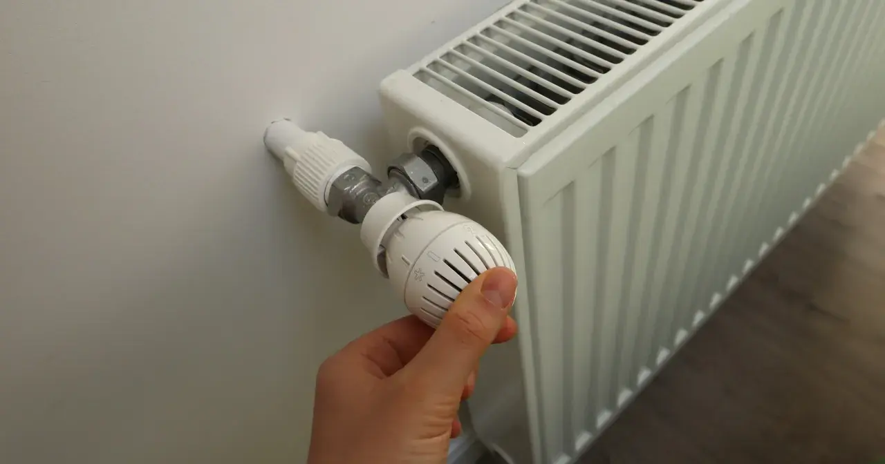 Dłoń reguluje termostat grzejnika. Sezon grzewczy od kiedy do kiedy zależy od pogody i przepisów.