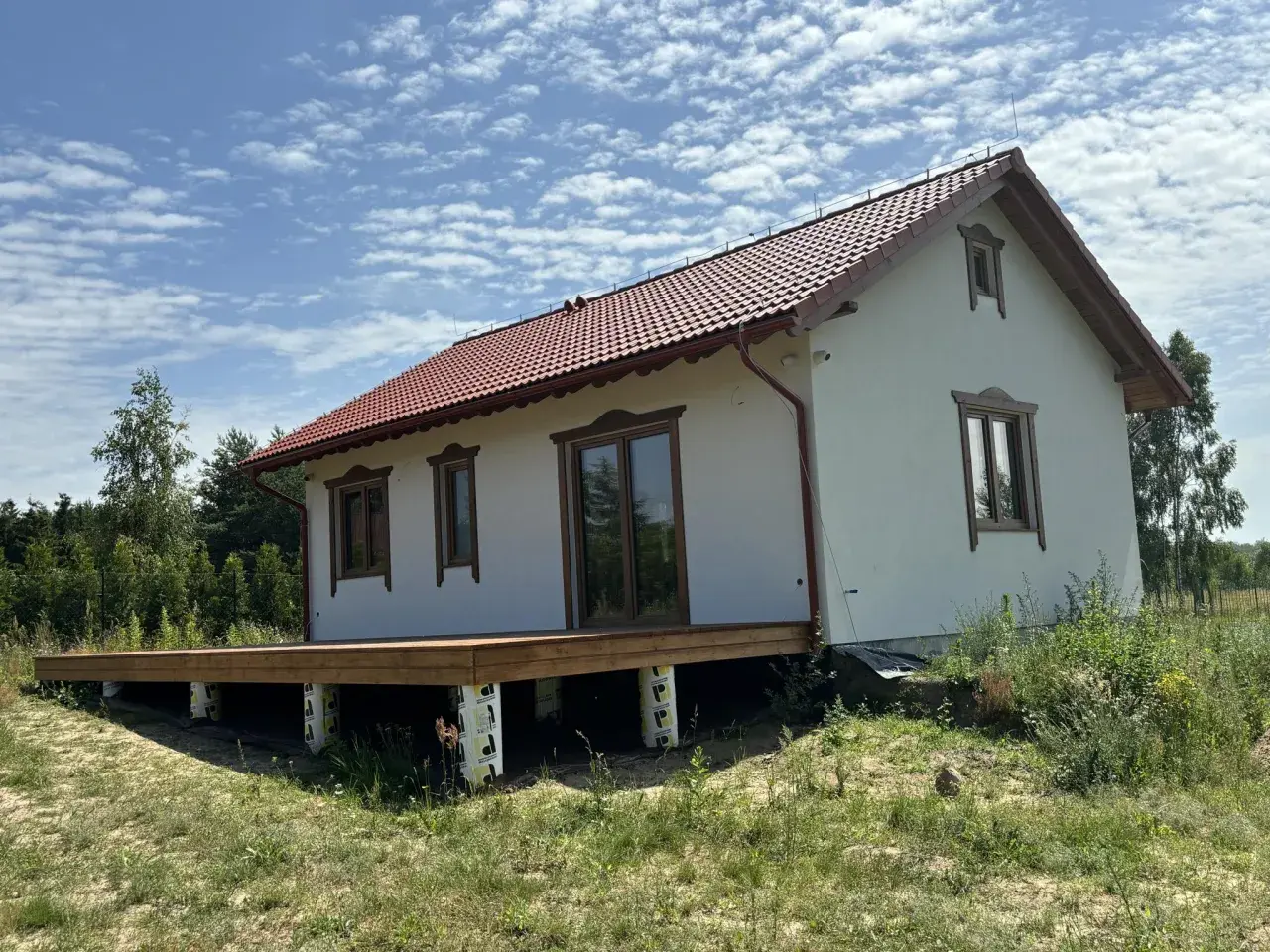 Nowy projekt domu drewnianego z tarasem, w otoczeniu zieleni.