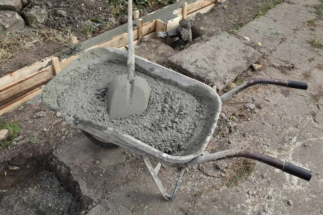Taczka z betonem i łopatą czeka na wykonanie zbrojenia ławy fundamentowej.