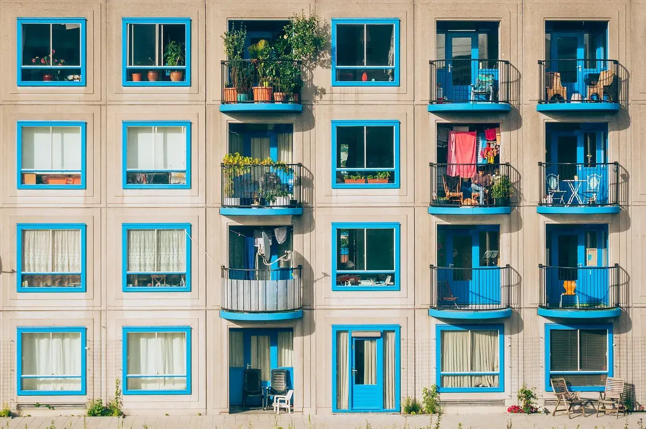 Elegancka loggia i balkon z niebieskimi ramami okiennymi, pełne zieleni i suszącego się prania, tworzą barwny obraz miejskiego życia.