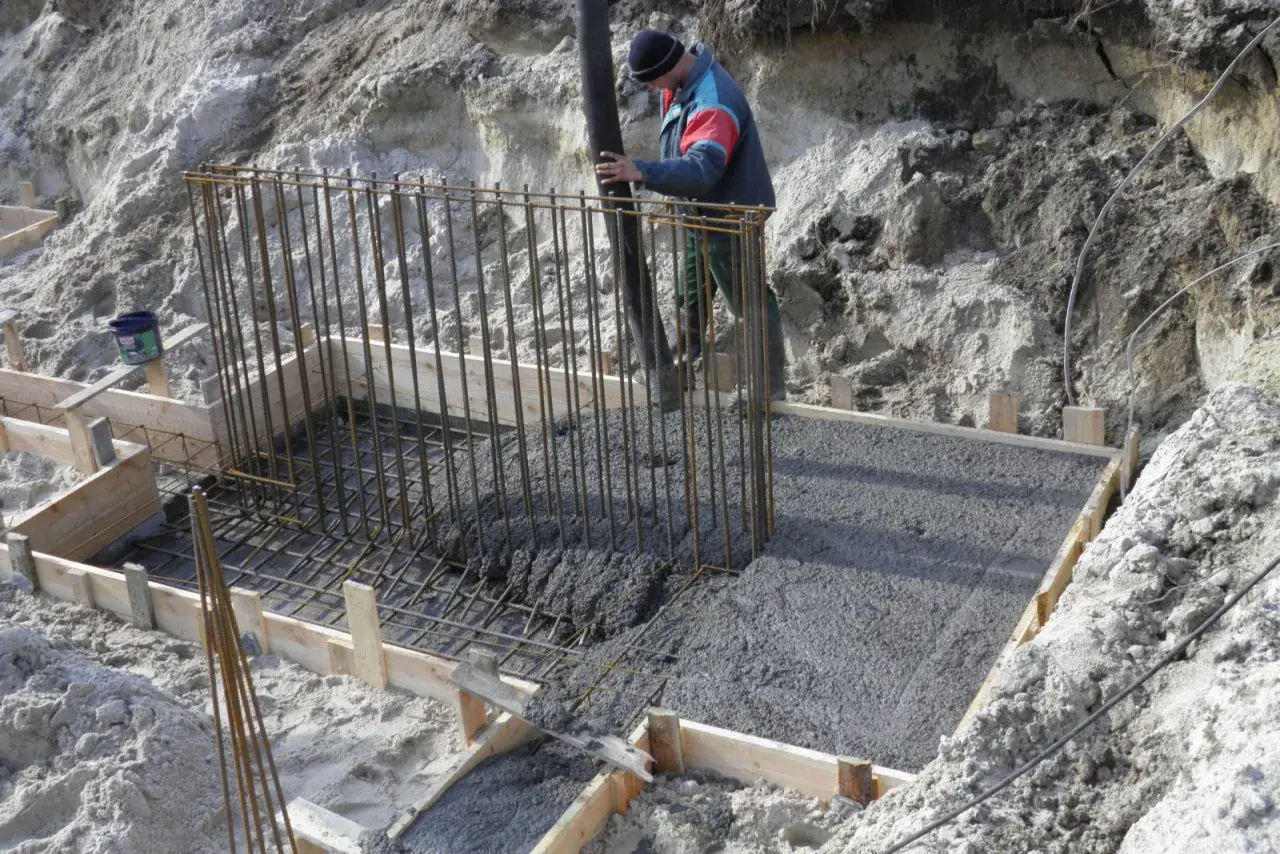 Betonowanie fundamentów. Pracownik wylewa beton do szalunku zbrojonego. Beton można lać do ok. +5°C.