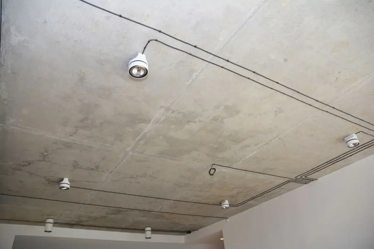 Nowoczesna instalacja elektryczna natynkowa na betonowym suficie z kilkoma białymi oprawami oświetleniowymi.