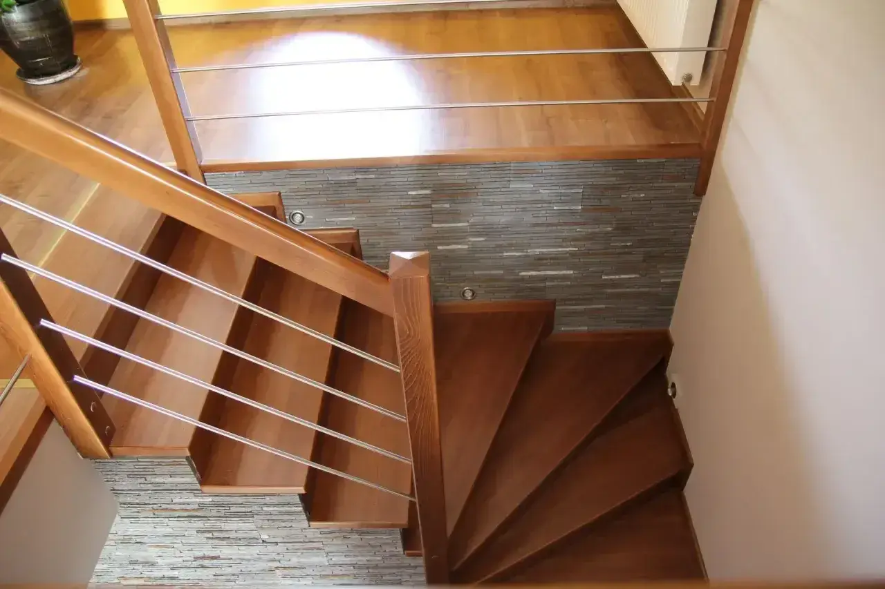 Eleganckie drewniane schody z metalową balustradą, prowadzące do górnego poziomu. Kamienna ściana stanowi stylowe tło, pokazując, jak zakończyć ostatni stopień schodów.