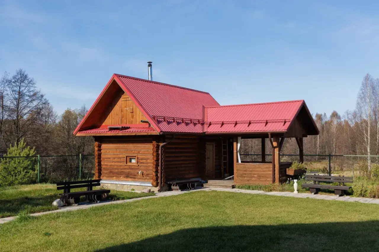Drewniany domek letniskowy z czerwoną dachem, idealny na wypoczynek. Marzysz o takim miejscu? Sprawdź możliwości dofinansowanie na domek letniskowy!