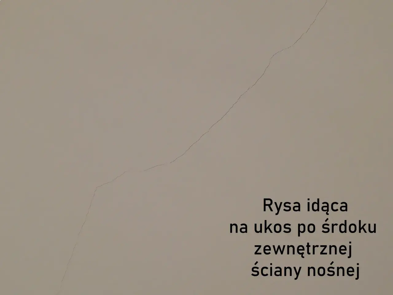 Pionowe pęknięcia ścian nośnych widoczne na jasnej powierzchni. Rysa biegnie ukośnie przez środek zewnętrznej ściany nośnej.