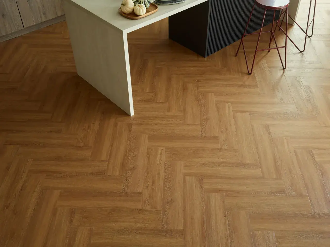 Drewnopodobne panele winylowe ułożone we wzór jodełki. Pokazują, jak układać panele winylowe, tworząc elegancką podłogę w kuchni.