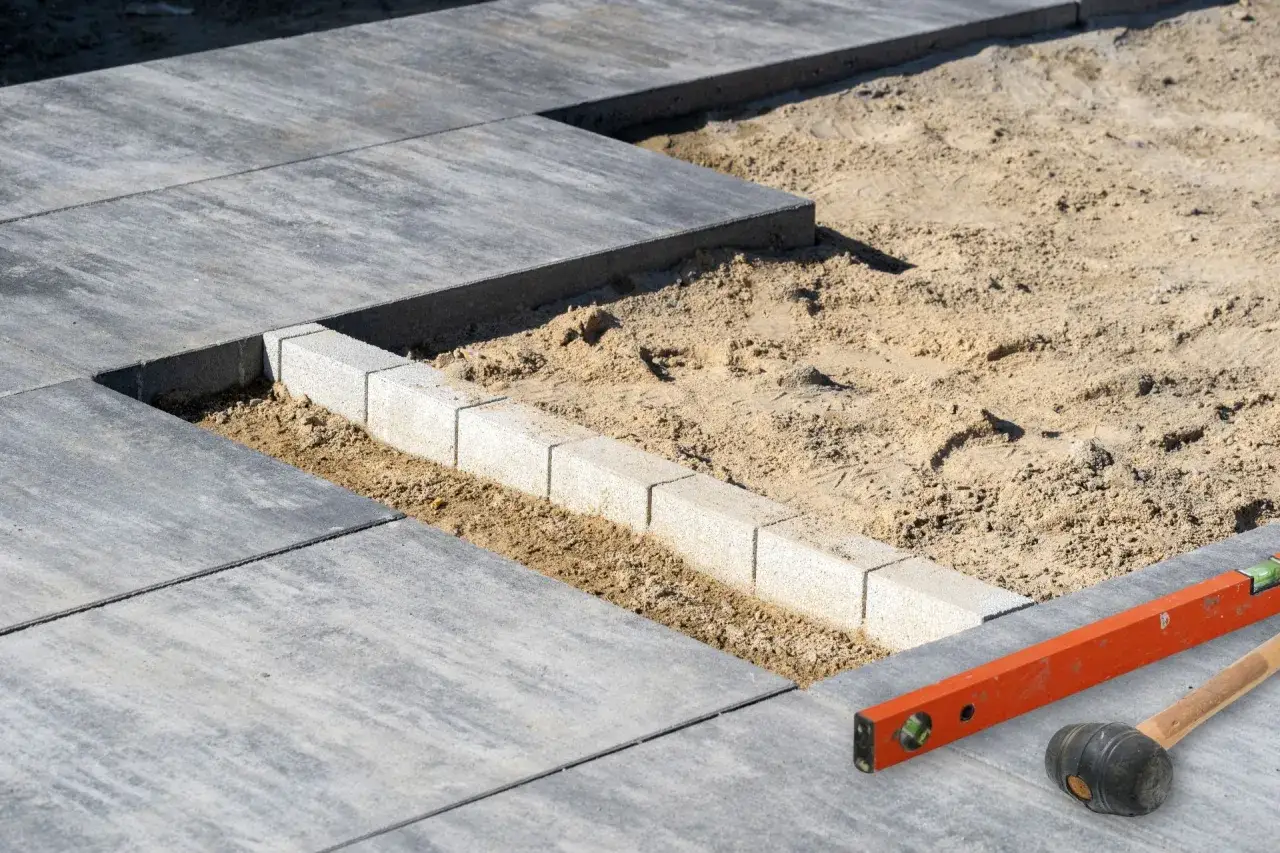 Układanie płyt tarasowych na suchym betonie. Widać poziomicę i gumowy młotek, narzędzia do precyzyjnego montażu.