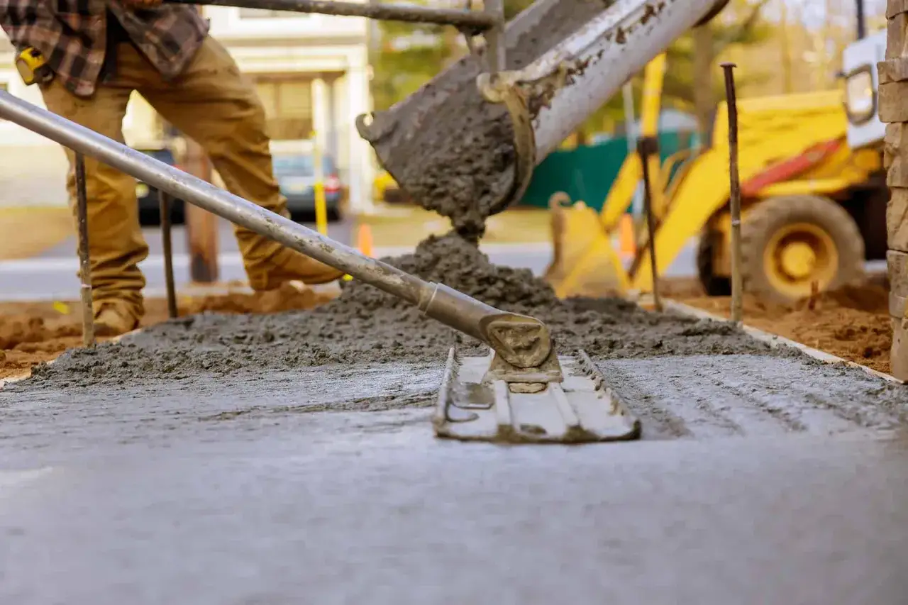 Pracownik wylewa beton, który będzie długo schnął w temperaturze 5 stopni. W tle koparka.